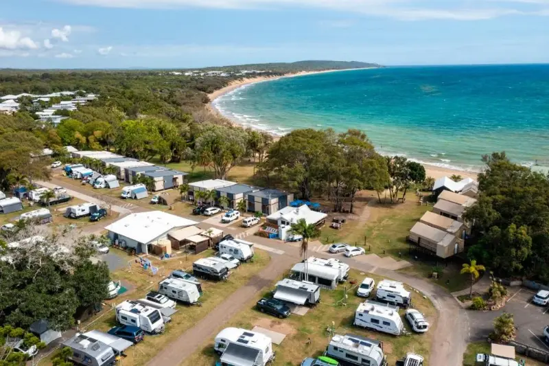 Aerial view of a caravan park beside a beach with a headland in the distance