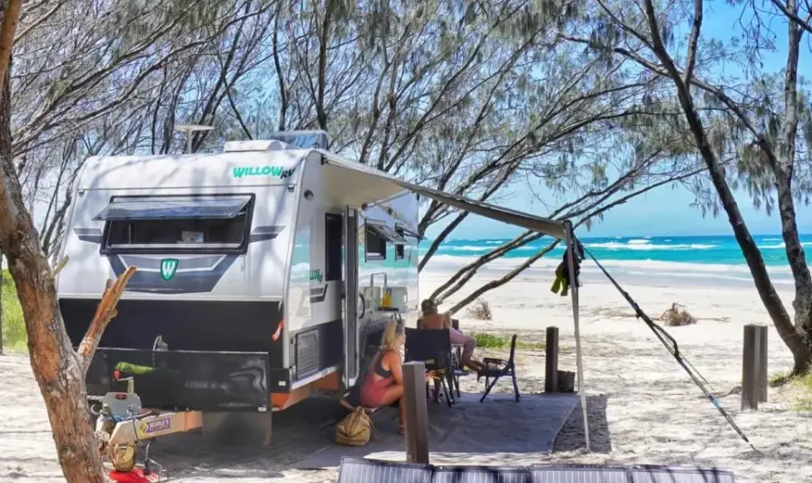 Willow RV caravan with awning out at a beachside campsite, couple relaxing in camp chairs